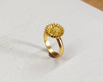 Könnte beinhalten: Ein goldener Ring mit einem Sonnenblumen-Design.