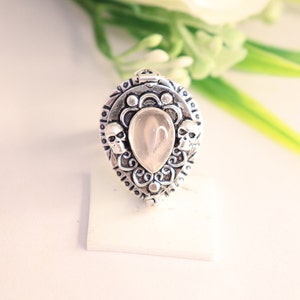 Puede incluir: Un anillo de plata con una piedra de cuarzo transparente y dos detalles de calavera. El anillo tiene forma de lágrima y un diseño intrincado.