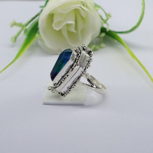 K&ouml;nnte beinhalten: Ein silberner Ring mit einem blauen und gr&uuml;nen Edelstein, der in einem filigranen Design eingefasst ist. Der Ring ist an einer Seite offen und hat einen Klappdeckel.