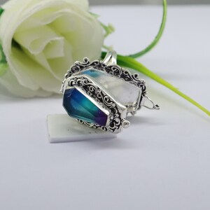 K&ouml;nnte beinhalten: Ein silberner Ring mit einem blauen und gr&uuml;nen Sarg-f&ouml;rmigen Stein. Der Ring ist ge&ouml;ffnet und der Stein ist sichtbar. Der Ring liegt auf einer wei&szlig;en Oberfl&auml;che.