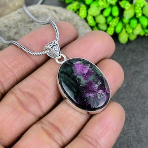 May include: A silver chain necklace with an oval-shaped pendant featuring a green and pink gemstone. The pendant has a detailed silver bail.