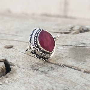 Può includere: Un anello d'argento con una pietra preziosa rossa incastonata in un design a filigrana decorativo.