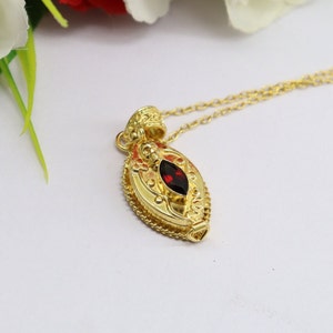 Peut inclure: Un collier en or avec un pendentif orné d'une pierre précieuse rouge dans un design détaillé et orné.