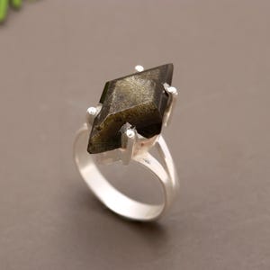 May include: A silver ring with a large, dark green, faceted gemstone set in a diamond shape.