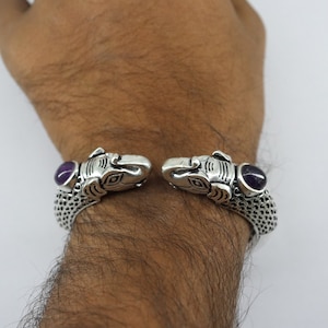 Könnte beinhalten: Silberarmband mit zwei Elefantenköpfen an jedem Ende, jeder Kopf hat einen violetten Edelstein in der Mitte.