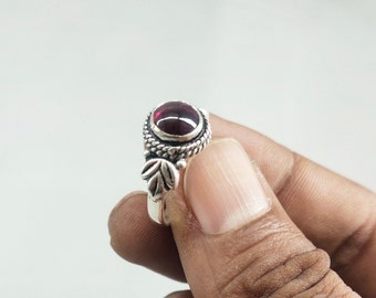 Può includere: Un anello d'argento con una pietra preziosa rosso scuro e dettagli a forma di foglie.