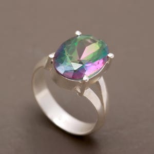 Könnte beinhalten: Ein silberner Ring mit einem großen, ovalen, schillernden Edelstein. Der Edelstein hat Farbtöne von Grün, Blau und Lila.