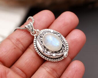 May include: A silver pendant necklace featuring an oval, iridescent moonstone. The moonstone is set in an ornate, detailed silver frame. The necklace is displayed on a hand, showcasing the jewelry's design and craftsmanship.