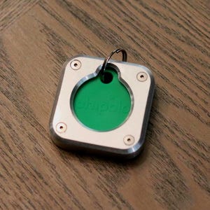May include: A square, silver-colored key finder with a green center and the word "chipolo" printed on it. The key finder has a metal ring for attachment and is secured with four small screws.
