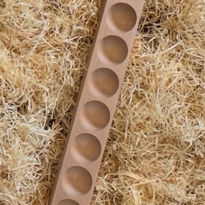 Op de afbeelding: Een houten eierhouder met acht cirkelvormige inkepingen. De houder is gemaakt van lichtgekleurd hout en staat op een achtergrond van versnipperde houtsnippers. De eierhouder is ontworpen om eieren veilig te bewaren.
