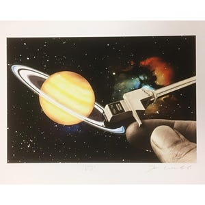 May include: Surreal art print depicting a yellow planet with rings against a starry backdrop. A silver record player needle is placed near the planet. The print includes the text "XL-150" and the artist's signature.