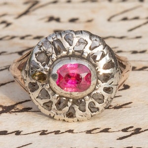 May include: A silver ring with a pink gemstone set in a circular bezel surrounded by a decorative silver design.