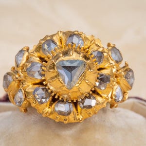 Könnte beinhalten: Ein goldener Ring mit einem großen, dreieckigen, facettierten, blauen Edelstein, umgeben von kleineren, facettierten, blauen Edelsteinen.