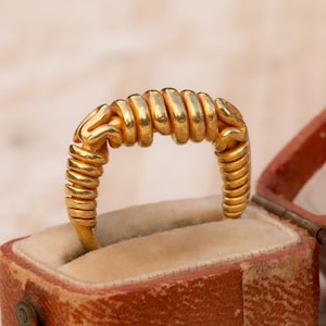 Op de afbeelding: Een gouden ring met een uniek opgerold ontwerp, gepresenteerd in een open vintage sieradendoosje. Het ingewikkelde patroon van de ring en de warme goudtint worden benadrukt.