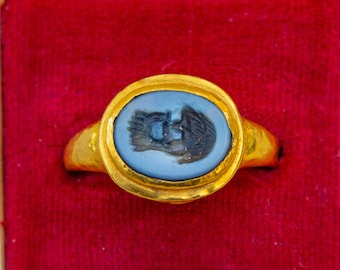 May include: A gold ring featuring a blue and black cameo set in a gold bezel. The cameo depicts a profile of a person.