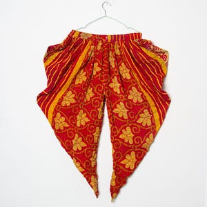 May include: Red and yellow patterned trousers hanging on a hanger. The trousers feature a floral design and striped accents. The fabric appears to be quilted. The trousers are a vibrant red with yellow floral and striped patterns.