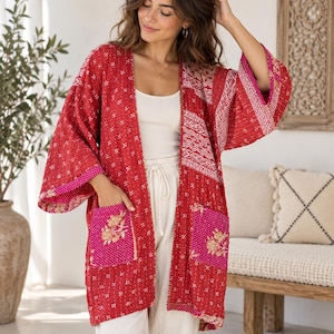 Könnte beinhalten: Eine rote, vorne offene Kimono-Jacke mit Patchwork-Design, weißen geometrischen Mustern und kontrastierenden leuchtend pinken Taschen, die mit goldener Blumenstickerei verziert sind. Das Kleidungsstück hat weite Dreiviertelärmel.