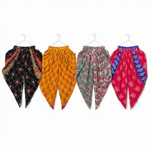 May include: Four pairs of colorful, patterned harem pants hanging on silver hangers. The pants feature various designs, including geometric and floral patterns, in shades of black, yellow, red, and green. The pants are made of a lightweight fabric.