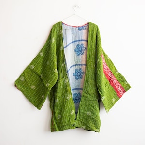 May include: A green kimono-style jacket with wide sleeves, hanging on a metal hanger. The jacket has a floral pattern on the inside lining, with red and white stripes on the sleeves. The outer layer is a textured green fabric.