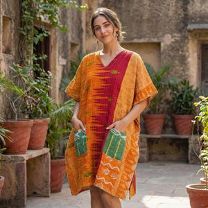 May include: A vibrant, knee-length tunic dress with a V-neck and short sleeves. The dress features a patchwork design in shades of orange, red, and green, with two front pockets. The fabric appears to be a lightweight, textured material.
