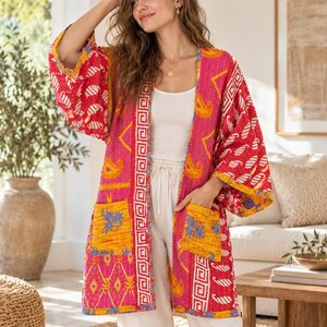Könnte beinhalten: Eine langärmelige, vorne offene Jacke mit einem lebendigen Patchwork-Design in den Farben Pink, Rot und Gelb. Das Kleidungsstück verfügt über zwei aufgesetzte Vordertaschen und ein weißes geometrisches Muster entlang der Öffnung und Ärmelbündchen.