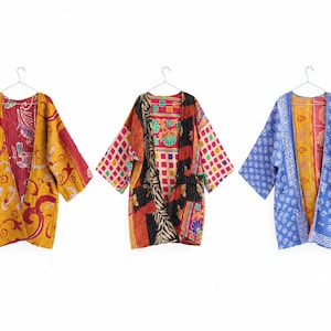 May include: Three open-front jackets hanging on hangers. The left jacket is yellow and red with floral patterns. The middle jacket features a patchwork design of black, white, red, and green squares. The right jacket is blue and white with floral prints.