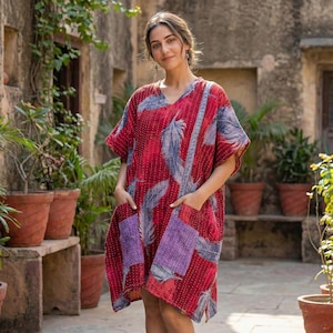May include: A red, short-sleeved dress with a V-neck and pockets. The dress features a feather pattern in blue and white, with purple pocket accents. The dress is knee-length and appears to be made of a soft, lightweight fabric.