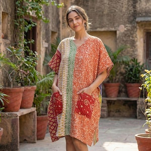 Op de afbeelding: Een kleurrijke, knielange jurk met een V-hals en korte mouwen. De jurk heeft een patchwork ontwerp met rode, oranje, groene en gele patronen. Het heeft twee voorzakken en een relaxte pasvorm, perfect voor casual wear.