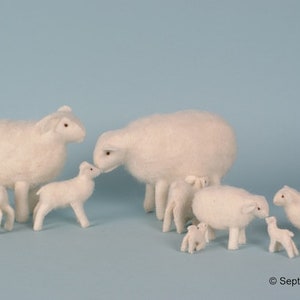 Puede incluir: Un grupo de ovejas de fieltro blanco, incluyendo una madre y su cordero, una oveja y su cordero, y un par de corderos. Las ovejas están todas de pie sobre un fondo azul claro.