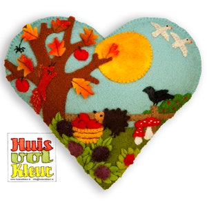 May include: A felt heart-shaped pillow with an autumn theme. The pillow features a brown tree with red apples, a squirrel, two white birds flying, a black bird, a yellow sun, and two hedgehogs. The pillow is surrounded by green leaves and red mushrooms.
