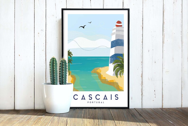 May include: A framed art print featuring a coastal scene with a lighthouse, ocean, and palm trees. The print has a blue and white lighthouse with a red top. The word "CASCAIS" is printed in white letters at the bottom.