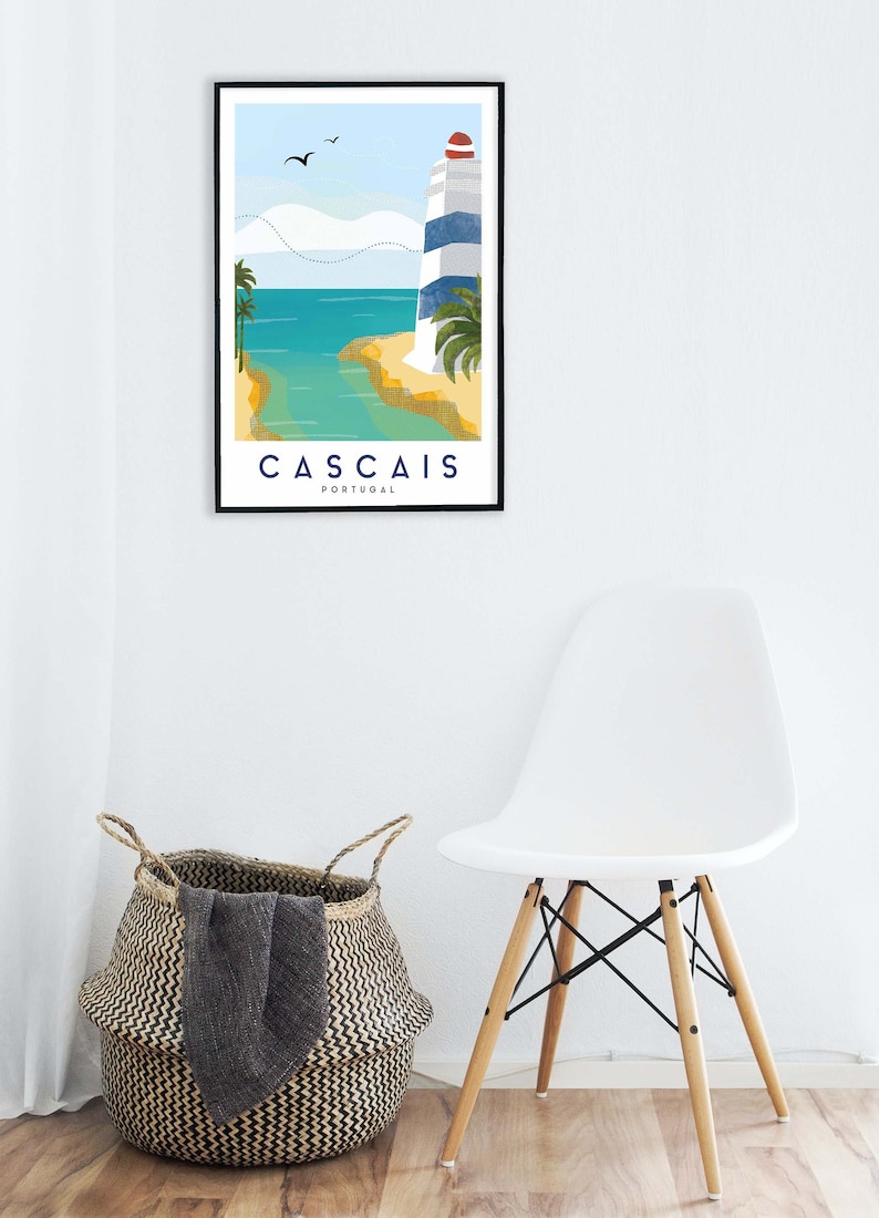 May include: A framed art print featuring a coastal scene of Cascais, Portugal. The artwork depicts a lighthouse with blue and white stripes, a sandy beach, and the text "Cascais Portugal". The print is in a black frame.