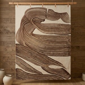 Puede incluir: Un tapiz rectangular con fondo color crema y grandes patrones abstractos de pinceladas en marrón oscuro. El tejido está suspendido de una barra de madera horizontal mediante correas de cuero sujetas al borde superior.