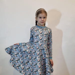 Könnte beinhalten: Ein blaues Kleid mit Blumen- und Hasenmuster. Das Kleid hat lange Ärmel und einen ausgestellten Rock.