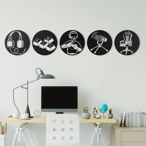 May include: Five black circular wall art pieces with white gaming icons: headphones, keyboard keys, a gamer with VR headset, a microphone, and a gaming chair. The art is displayed above a desk with a computer.