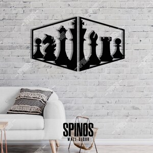 May include: Black metal wall decor featuring a chess piece design. The design is in the shape of a cube with chess pieces on each side. The wall decor is mounted on a white brick wall.