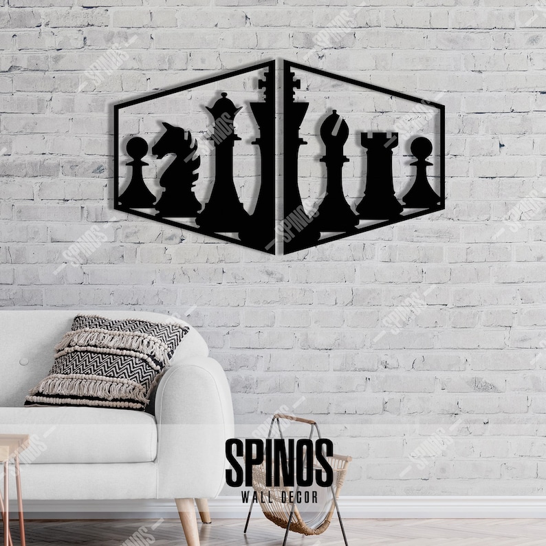 May include: Black metal wall decor featuring a chess piece design. The design is in the shape of a cube with chess pieces on each side. The wall decor is mounted on a white brick wall.