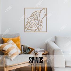May include: A brown tribal wolf head silhouette wall decal in a square frame. The decal is on a white wall above a light gray couch with pillows. The text "SPINOS WALL DECOR" is on a wooden table in front of the couch.