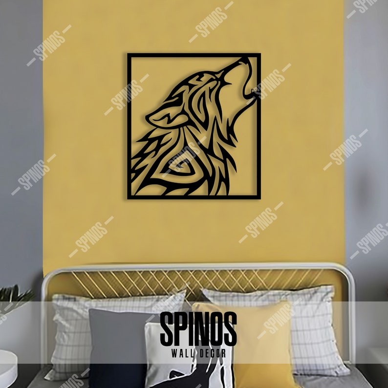 May include: Black metal wall decor featuring a stylized wolf howling at the moon. The wolf is in a square frame against a yellow wall. The image also shows a bed with pillows in the foreground.