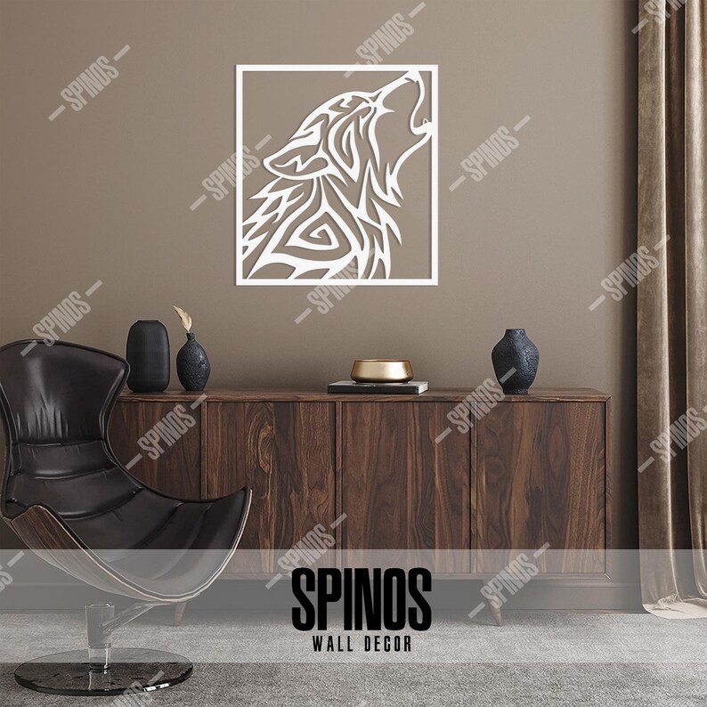 May include: White wooden wall decor featuring a stylized wolf howling at the moon. The wolf is in a square frame and is set against a brown wall. The decor is displayed on a wooden shelf with a black chair and two vases.