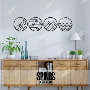 May include: Four black metal wall decor circles with different designs: fire, wind, mountains, and water. The circles are arranged in a row on a white wall above a wooden dresser. The text "SPINOS WALL DECOR" is displayed below the dresser.