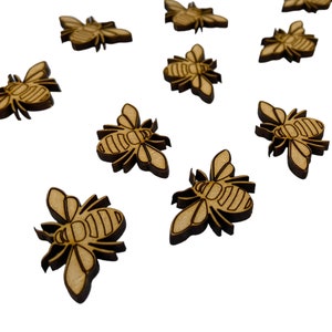 May include: A scattering of small, wooden bee-shaped cutouts. Each bee has detailed wing and body designs, with a light brown colour and darker brown outlines. These decorative wooden bees are scattered across a white background.