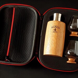 Pode incluir: Um conjunto de whisky numa caixa preta com fecho vermelho. O conjunto inclui uma garrafa de madeira, dois copos e o texto "Irish Whiskey". A garrafa e os copos têm uma base de madeira.