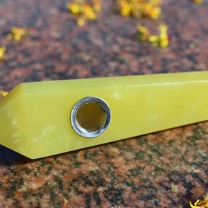 Könnte beinhalten: Eine gelbe Kristallpfeife mit einem Metallkopf. Die Pfeife ist glatt und poliert, und der Kopf ist rund und hat ein kleines Loch in der Mitte.