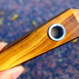 May include: A golden tiger's eye crystal pipe with a metal screen. The pipe is shaped like a point and has a natural wood grain.