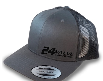 Può includere: Cappellino da camionista grigio e nero con un logo ricamato nero che dice "24 VALVE TURBO DIESEL". Il cappello ha una parte posteriore in rete nera e una parte anteriore grigia con un adesivo argentato che dice "THE AUTHENTIC SNAPBACK YUPOONG SINCE 1974".
