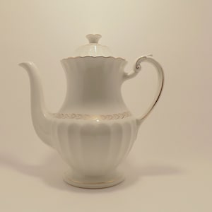 May include: White porcelain coffee pot with a gold trim and a lid. The pot has a fluted design and a curved handle.