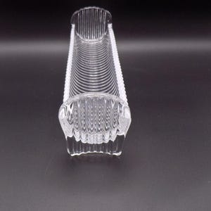 May include: A clear, rectangular glass dish with a ribbed interior and scalloped edges. The dish has a curved shape and is designed to hold items. The glass is transparent, allowing light to pass through.