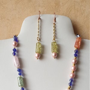 May include: A multi-colored beaded necklace with pink, green, blue, and yellow rectangular beads. The necklace is paired with matching earrings with green rectangular beads.