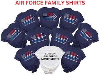 Op de afbeelding: Een set van marineblauwe t-shirts met een Amerikaans vlagontwerp en de tekst "Proud Air Force" met verschillende familieleden-titels. De shirts zijn in een cirkel gerangschikt met een wit t-shirt in het midden waarop "Custom Air Force Family Shirts" staat.